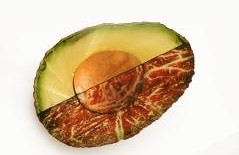 Eine Avocadohälfte, die Hälfte davon ist grün, die andere weißt eine rote fleischähnliche oder hölzerne Struktur auf.