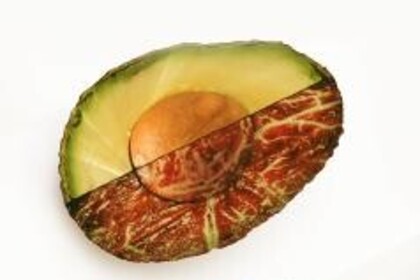 Eine Avocadohälfte, die Hälfte davon ist grün, die andere weißt eine rote fleischähnliche oder hölzerne Struktur auf.