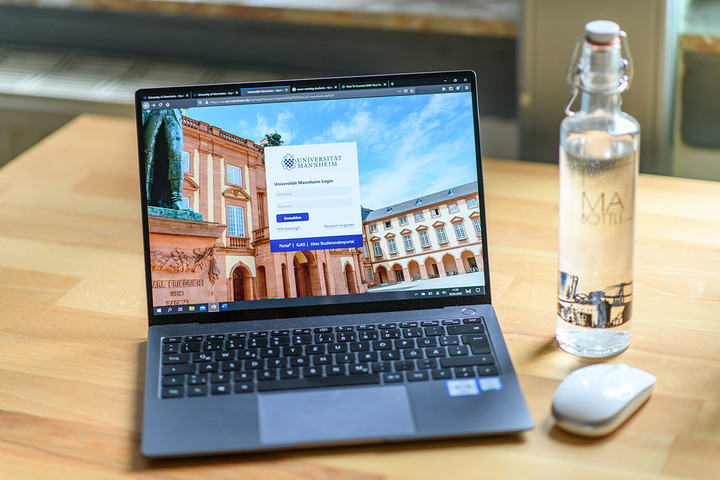 Ein Laptop, eine Maus und eine Wasserflasche stehen auf einem Tisch.