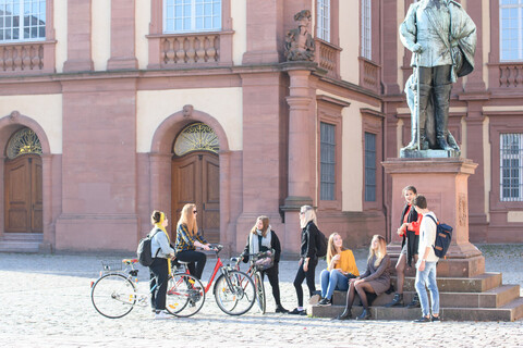 Eine Gruppe aus Studierenden versammelt sich um das Karl-Ludwig-Denkmal vor dem Schloss.