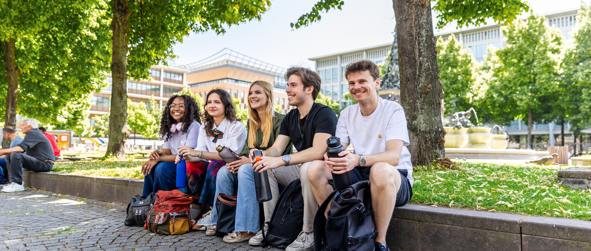 Eine Gruppe von fünf Studierenden sitzen an einem sonnigen Tag am Paradeplatz. Sie scheinen glücklich zu sein und gute Laune zu haben.
