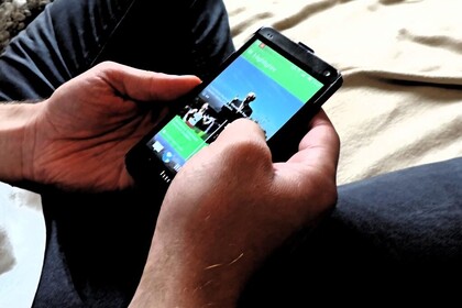 Eine Person sitzt auf einer Decke und hält ein Handy mit zu sehenden Fotos in ihren Händen.