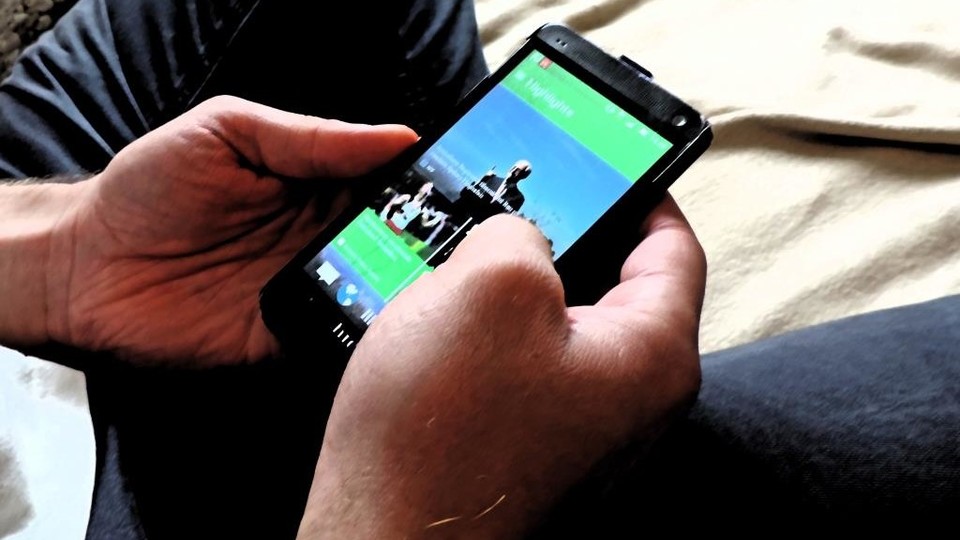 Eine Person sitzt auf einer Decke und hält ein Handy mit zu sehenden Fotos in ihren Händen.