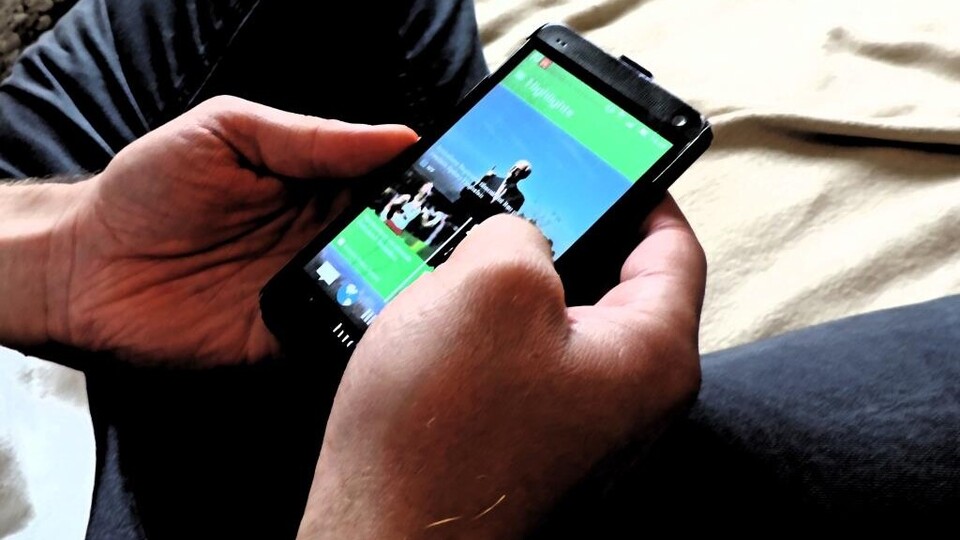 Eine Person sitzt auf einer Decke und hält ein Handy mit zu sehenden Fotos in ihren Händen.