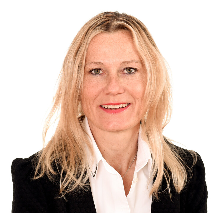 Portrait von Sabrina Scherbarth. Sie trägt eine weiße Bluse sowie einen schwarzen Blazer und lächelt.