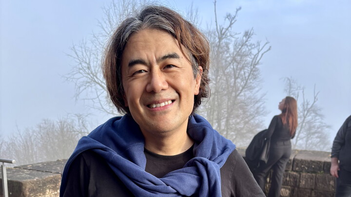 Charles Yang trägt ein schwarzes T-Shirt, über den Schultern hat er einen blauen Pullover.