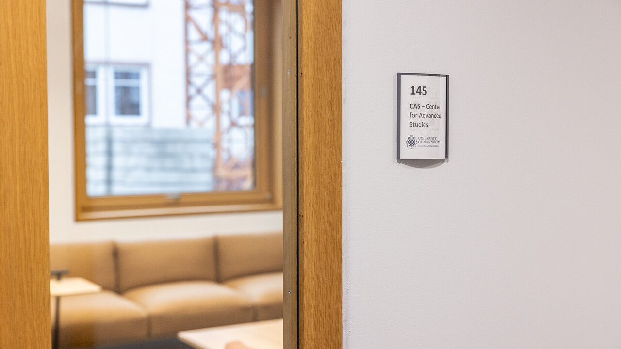 Man sieht ein Türschild des CAS und den Bick auf eine Sitzgruppe in einem Raum.