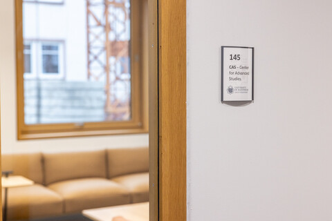Man sieht ein Türschild des CAS und den Bick auf eine Sitzgruppe in einem Raum.