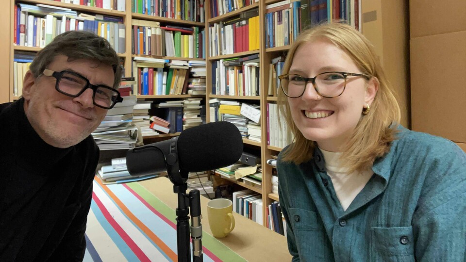 Ein Mann und eine Frau mit Mikrofon an einem Tisch vor Bücherregalen
