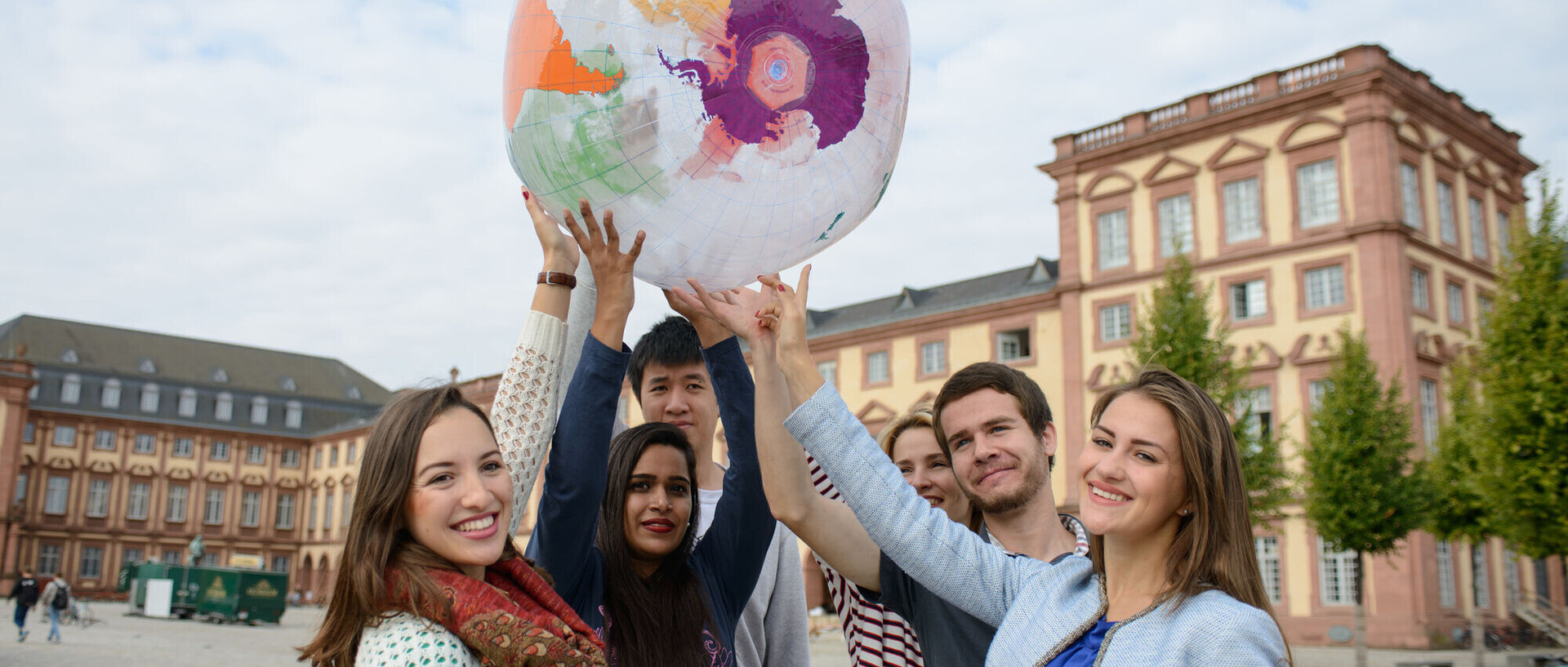 Sechs internationale Studierende halten gemeinsam eine aufblasbare Weltkugel auf dem Ehrenhof der Uni in die Luft