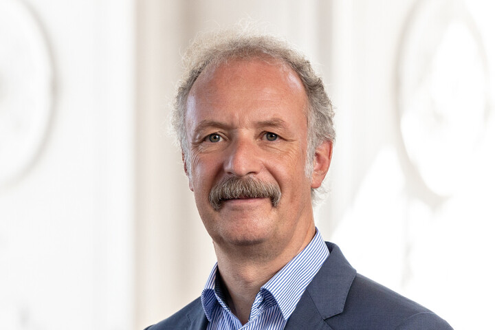 Prof. Dr. Moritz Fleischmann hat graue Haare und einen Schnauzer. Er trägt ein dunkles Jackett und ein gestreiftes Hemd.