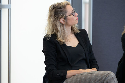 Ashley Metz trägt ein schwarzes Top sowie einen schwarzen Blazer und blickt nach links.