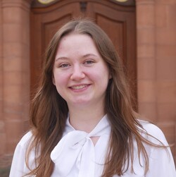 Anna-Lena Peitz has straight brown hair. She is wearing a white blouse with a bow.