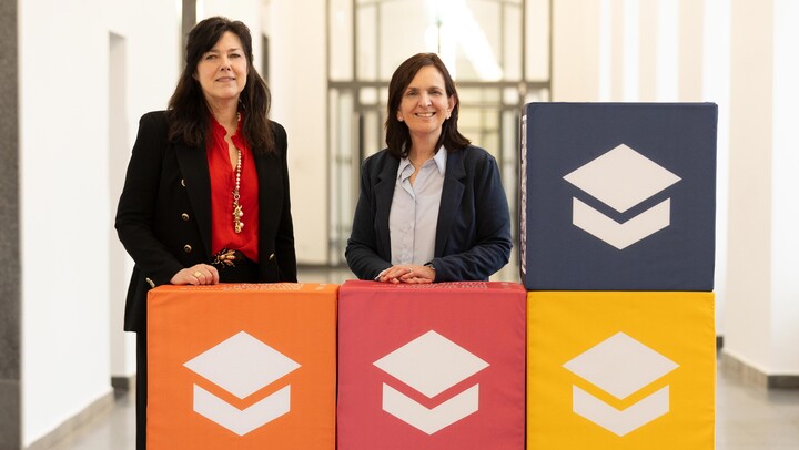 Betty Kübe und Maria Collado stehen hinter bunten Würfeln mit dem Logo der Universität Mannheim Service und Marketing GmbH.