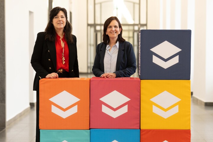 Betty Kübe und Maria Collado stehen hinter bunten Würfeln mit dem Logo der Universität Mannheim Service und Marketing GmbH.