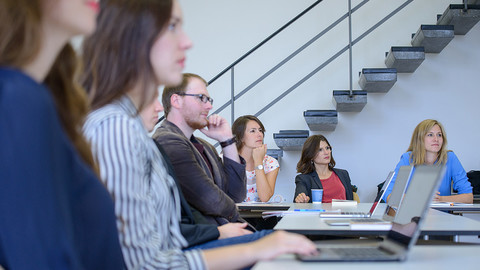 Junge Frauen und Männer sitzen mit ihren Laptops in einem Seminarraum.