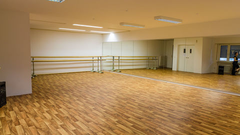 Einladender Tanzraum mit Parkettboden und Ballettstangen im Hintergrund; das Licht ist freundlich und hell.
