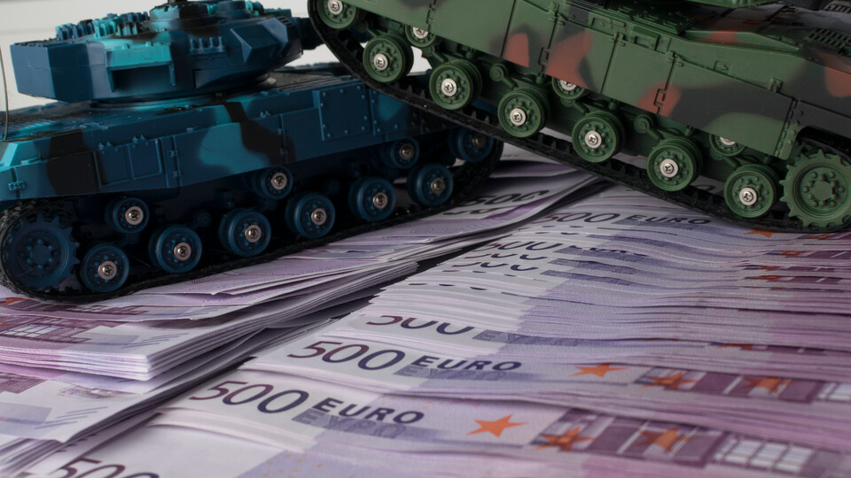 Zwei Spielzeugpanzer auf gestapelten 500-Euro-Scheinen.