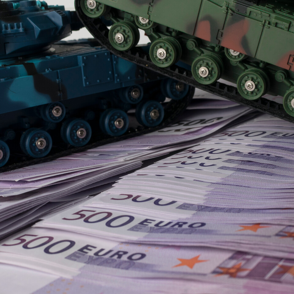 Zwei Spielzeugpanzer auf gestapelten 500-Euro-Scheinen.