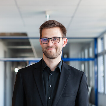 Dr. Stefan Janke hat kurze braune Haare und einen Dreitagebart. Er trägt ein schwarzes Hemd, einen schwarzen Sakko und eine schwarz umrandete Brille.