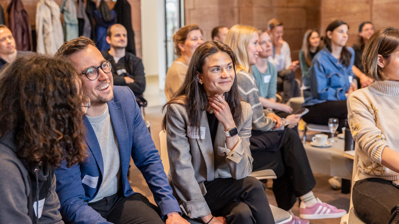 Personen sitzen in den Katakomebn des Schlosses in lockerer Runde und hören aufmerksam zu. Drei Personen im Vordergrund blicken lächelnd in eine Richtung.