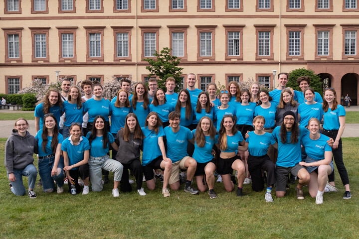 Die Studierenden der Fachschaft Psychologie stehen mit blauen T-Shirts auf der Mensawiese und lächeln in die Kamera.