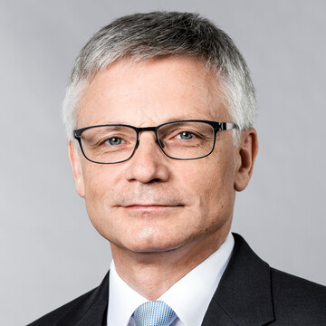 Georg Müller hat kurze graue Haare. Er trägt eine Brille, einen schwarzen Anzug und ein helles Hemd