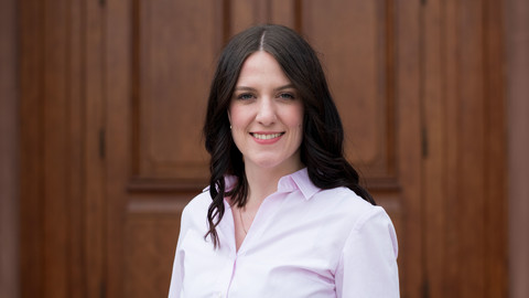 Marilena Adleff. She is wearing a white shirt and is standing in front of one of the castle doors.