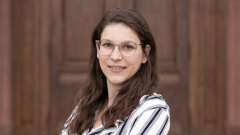 Carolina Möhringer. She is wearing a black-white stripped blouse and is standing in front of a brown door.