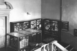 schwarz-weiß Aufnahme des Treppenflurs der Universität Mannheim. An den Wänden stehen Regale mit Ausstellungen.