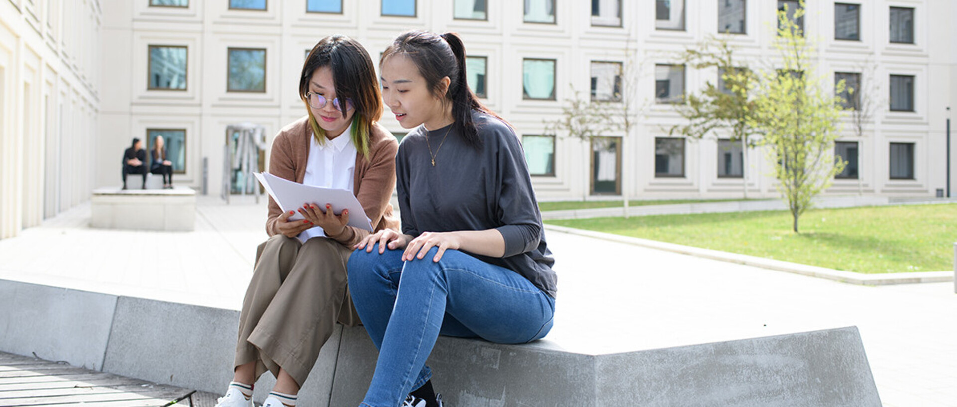 Two students are sitting and talking in the B6, 30-32 courtyard about doctoral studies.