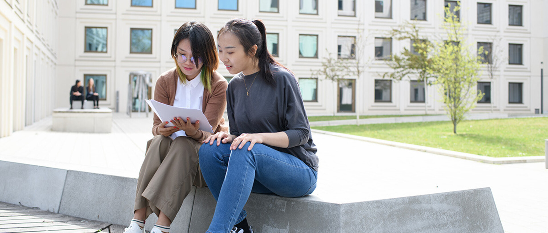 Two students are sitting and talking in the B6, 30-32 courtyard about doctoral studies.