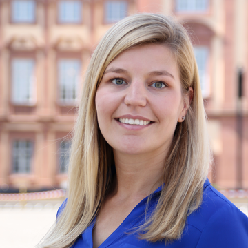 Lea Bastian steht in einer blauen Bluse auf dem Ehrenhof