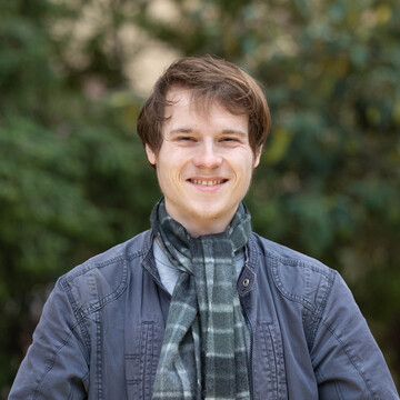  Paul Heierling. Er lächelt und trägt einen grünlich karierten Schal über einer grauen Jacke.