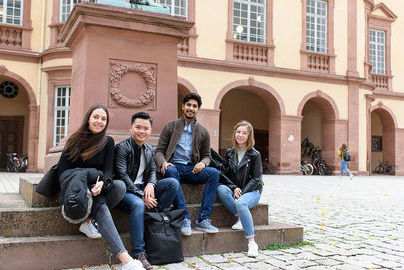 Vier Studierende sitzen auf den Treppenstufen der Karl Friedrich Statue auf dem Ehrenhof der Uni Mannheim