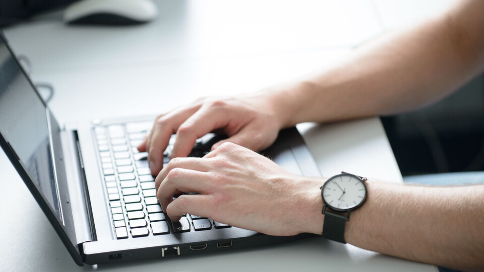 aufgeschlagener Laptop mit zwei Händen an der Tastatur, am rechten Handgelenk befindet sich eine Armbanduhr.