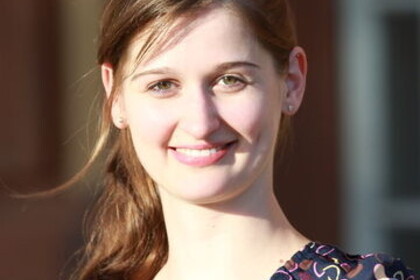 Franziska Bott hat ihre langen braunen Haare zu einem Zopf gebunden. Sie trägt ein buntes Oberteil und lächelt in die Kamera.