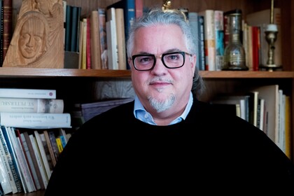 Porträt von Michael Meckel. Er trägt eine schwarze Brille und einen dunklen Pullover und schaut freundlich in die Kamera. Hinter ihm befindet sich ein Bücherregal.