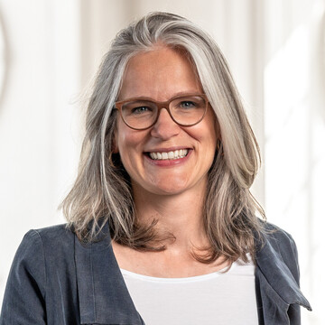 Frau Prof. Jutta Mata hat graue halblange Haare, sie trägt eine braune Brille und einen grauen Blazer.