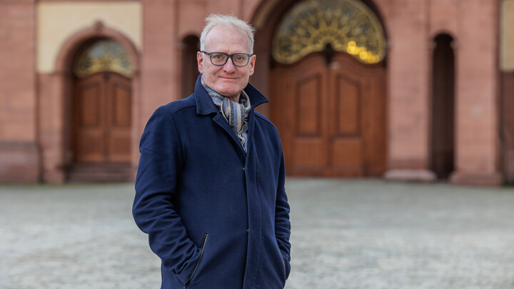 Portraitfoto von Prof. Dr. Matthias Kohring vor dem Schloss Mannheim. Er trägt einen dunkelblauen Mantel.