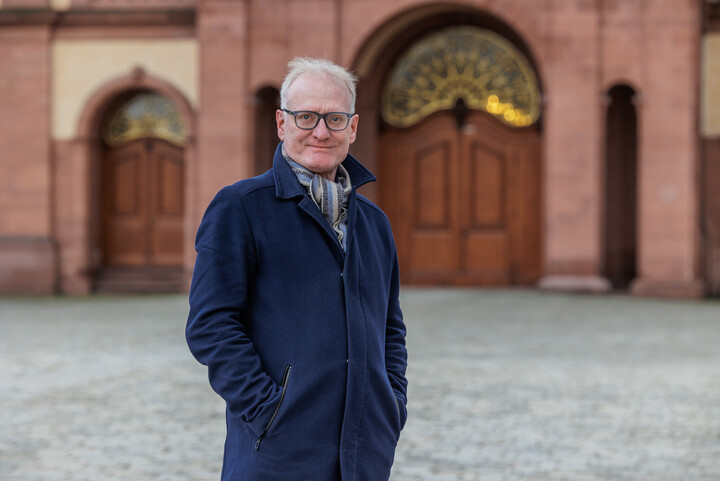 Portraitfoto von Prof. Dr. Matthias Kohring vor dem Schloss Mannheim. Er trägt einen dunkelblauen Mantel.