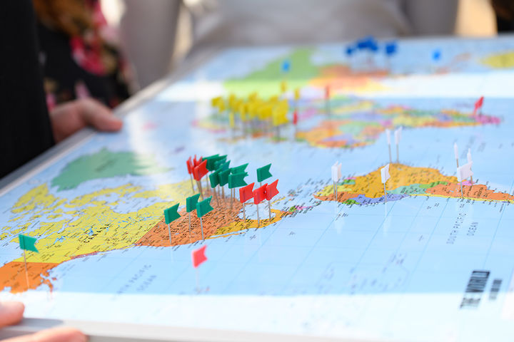 Mehrere bunte Stecknadeln stecken auf einer Weltkarte.