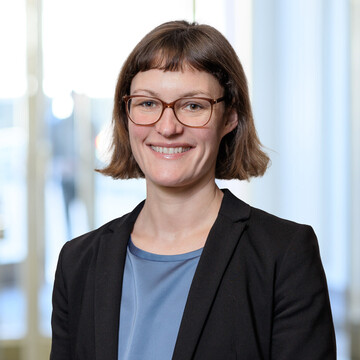 Katharina Nicol trägt ein dunkelblaues Oberteil und darüber einen schwarzen Blazer. Sie lächelt in die Kamera.