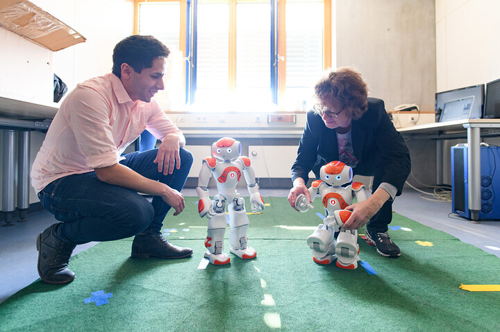 Eine Frau und ein Mann knien hinter zwei kleinen Robotern
