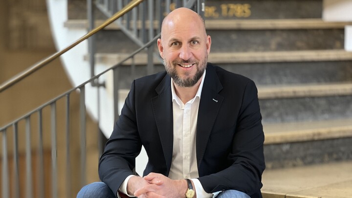 Patrick Barth sitzt auf einer Treppe im Schloss Mannheim. Er trägt ein weißes Hemd, ein schwarzes Sakko und eine Jeans.