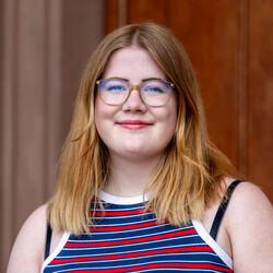 Mila Revink. Sie trägt schulterlange Haare und Brille und lächelt freundlich in die Kamera.