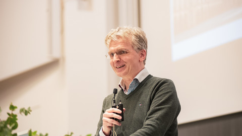 Prof. Dr. Justus Fetscher spricht auf einer Bühne mit einem Mikro in der Hand