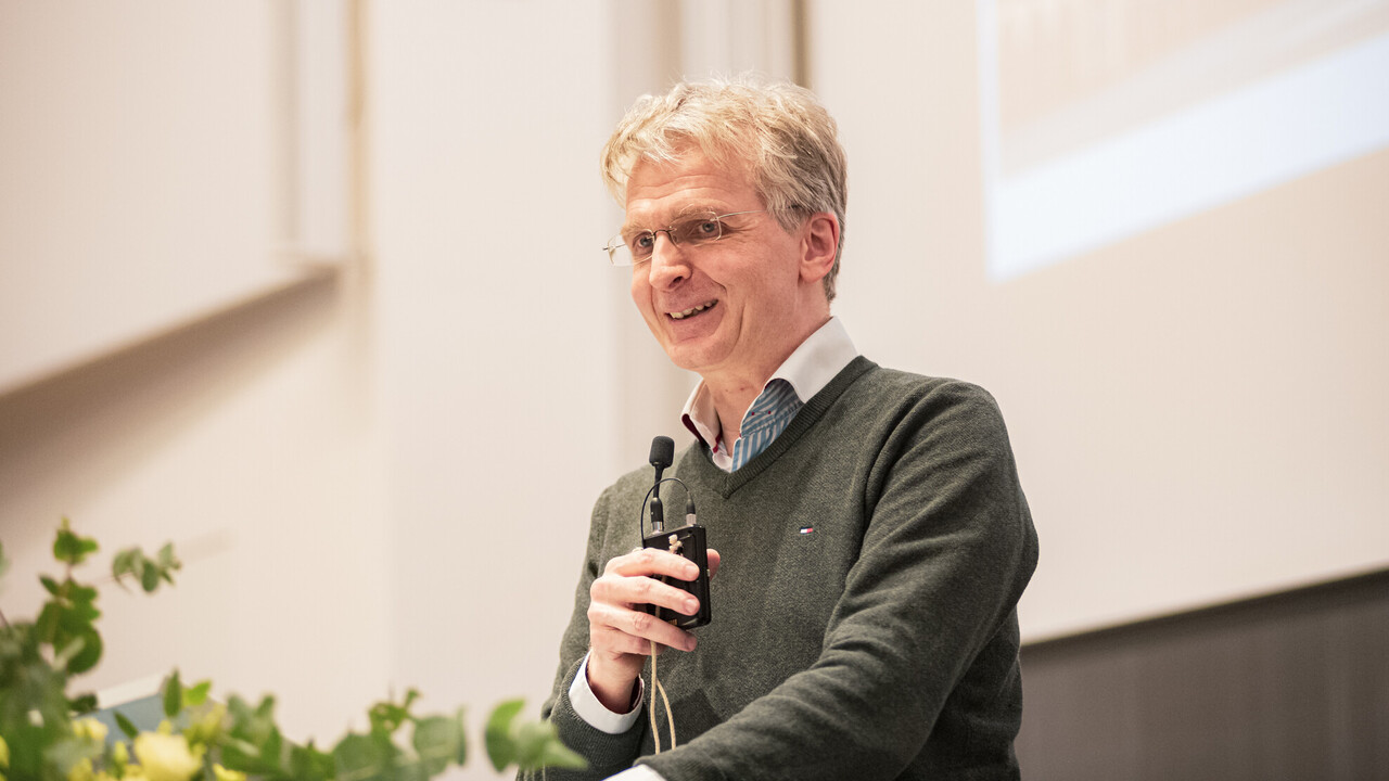 Prof. Dr. Justus Fetscher spricht auf einer Bühne mit einem Mikro in der Hand