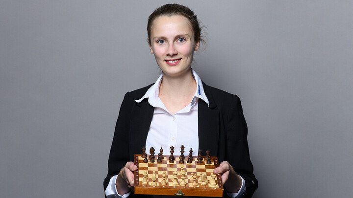 Eine lächelnde Person trägt eine weiße Bluse sowie einen schwarzen Blazer und hält ein Schachbrett in den Händen. Die Person heißt Josefine Heinemann.