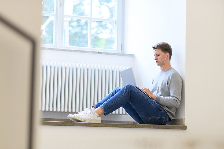 Ein Student sitzt auf einer Fensterbank und arbeitet am Laptop. 